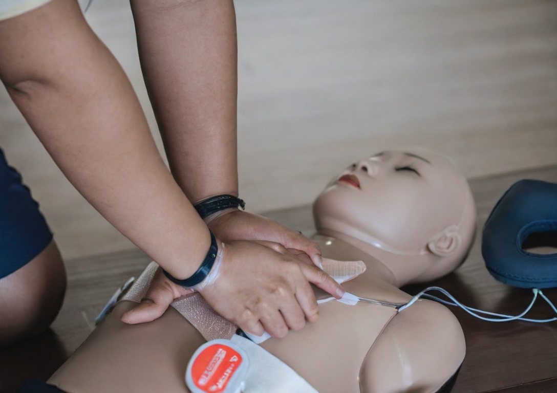 Hands performing CPR chest compressions on a training manikin with AED pads applied